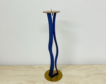 May include: A blue metal candle holder with a gold base. The holder is shaped like a wave and has a single candle holder on top.
