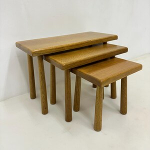 Può includere: Un set di tre tavolini in legno nidificati con finitura naturale. I tavolini sono rettangolari e hanno un design semplice con quattro gambe ciascuno.