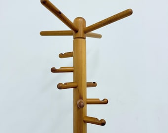 Può includere: Un attaccapanni in legno marrone chiaro con più ganci e un design a stella nella parte superiore. L'attaccapanni ha un palo centrale con diversi ganci orizzontali per appendere oggetti. La parte superiore ha più bracci che si estendono verso l'esterno.