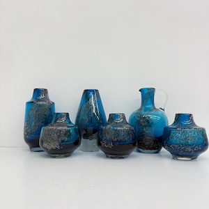 May include: A collection of seven decorative glass vases in various shapes and sizes. The vases display a striking blue and black colour scheme with textured patterns. Some have a glossy finish, others appear matte. A pitcher with a handle is also included.