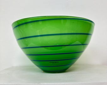 May include: A green glass bowl with blue stripes. The bowl is made by Kosta Boda.
