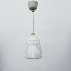 May include: White pendant light fixture with a textured, bell-shaped shade. The shade features a ribbed lower section and a diamond pattern on the upper portion. The fixture includes a gray ceiling mount and a clear crystal accent.