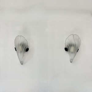 Puede incluir: Un par de apliques de pared de vidrio esmerilado con un diseño en forma de concha. Las apliques están montadas en una pared blanca.