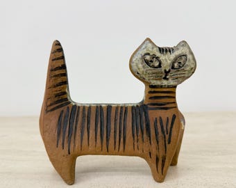 Op de afbeelding: Een keramieken kattenbeeldje met een bruin lichaam en zwarte strepen. De kat heeft een gedetailleerd gezicht met een lichtbruin en wit kleurenschema. De staart staat omhoog en het beeldje staat op vier poten.