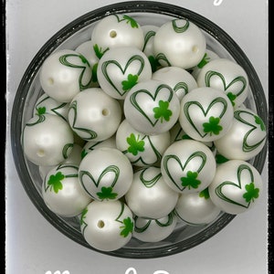 May include: White round beads with green shamrock and heart designs. The beads are in a clear glass bowl. The text "St. Patricks Day" is at the top of the image and "Mama Jo Designs" is at the bottom of the image.