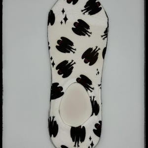 May include: White no-show socks with a repeating pattern of black winged creatures with red eyes and small diamond shapes. The socks have a low-cut design with a cushioned heel and toe.