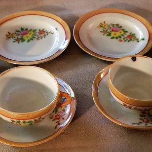 May include: A set of miniature teacups and saucers with floral patterns. The cups and saucers are white with gold trim and feature delicate floral designs in shades of pink, yellow, and green.