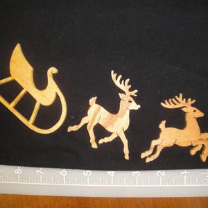 May include: Three wooden cutouts of a sleigh, a reindeer, and a deer. The sleigh is brown and has a curved design. The reindeer and deer are brown and have antlers.