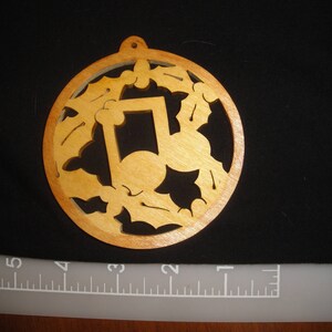May include: A wooden ornament shaped like a musical note surrounded by holly leaves. The ornament is painted in shades of brown and has a rustic look.