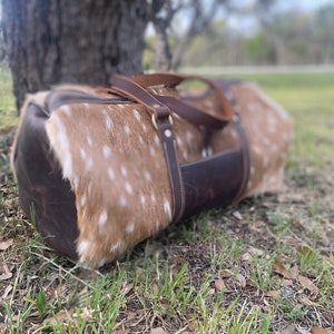 May include: A brown leather duffel bag with a spotted pattern. The bag has two brown leather straps and a brass buckle.