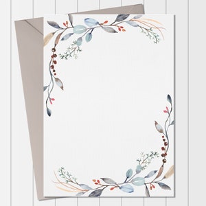 May include: A white card with a watercolor border of blue and green leaves and red berries. The border is on the top and right sides of the card. The card is on a white wood background.