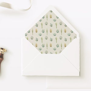 May include: A white envelope with a cactus and succulent pattern lining the inside flap. The envelope is lying open on a white surface with a wax seal next to it.