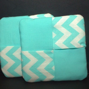 May include: Two turquoise blue fabric pot holders with a white chevron pattern. The pot holders are made of a soft, quilted fabric.