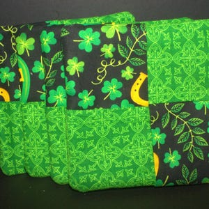 May include: Four green and black fabric coasters with a shamrock and horseshoe design. The coasters are made of a patchwork of different fabrics.