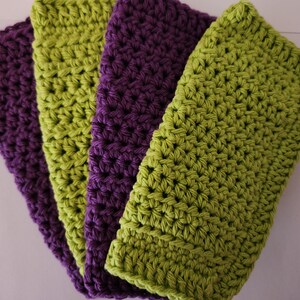 May include: Four crocheted dishcloths, two green and two purple, are stacked on top of each other.