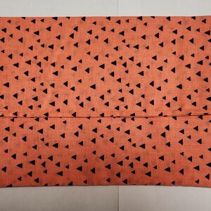 May include: A coral-colored fabric envelope with a black triangle pattern. The envelope is folded in half and has a seam down the center.