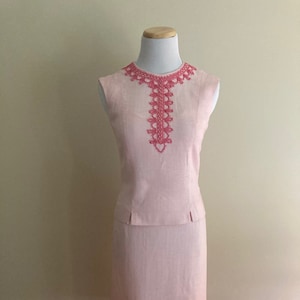 Peut inclure: Une robe rose sans manches avec une bordure en dentelle rose et blanche autour de l'encolure. La robe a un corsage ajusté et une jupe droite.