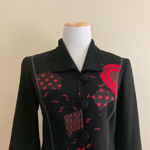 May include: A black cropped jacket with red and black geometric designs. The jacket has a collar and button closure.