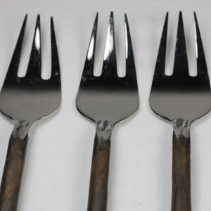 May include: Three silver forks with rust-colored handles. The forks are arranged in a row, with the tines facing up.