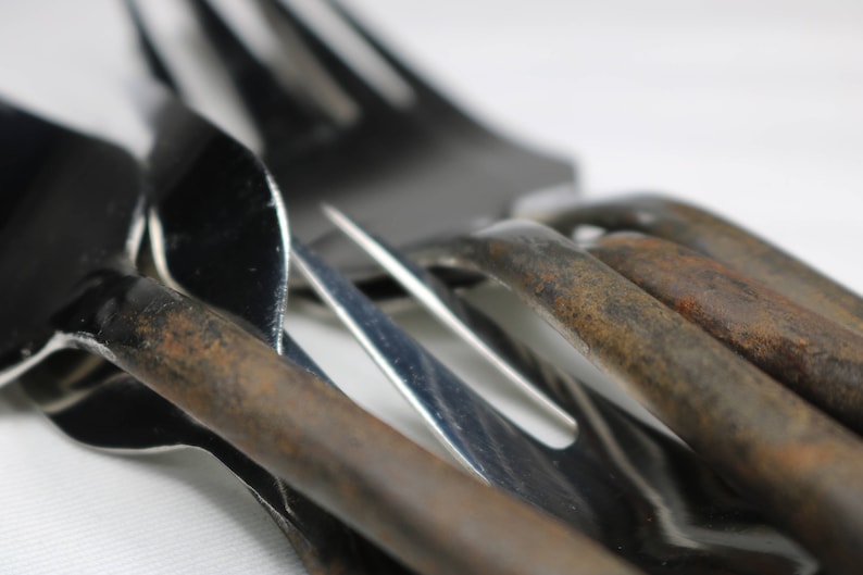 May include: A close-up of a set of silverware, including a fork, a spoon, and a knife. The silverware is made of metal and has a shiny finish. The silverware is arranged in a way that shows off its details.