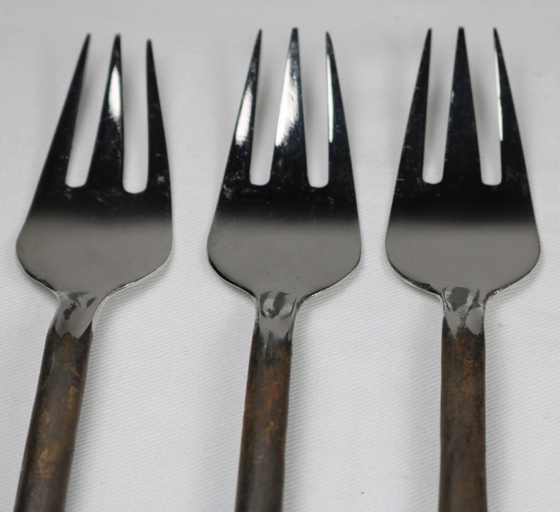 May include: Three silver forks with rust-colored handles. The forks are arranged in a row, with the tines facing up.