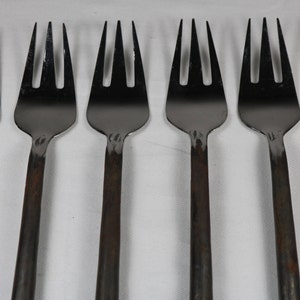 May include: Six silver forks with black handles. The forks are arranged in a row, with the handles pointing to the right.
