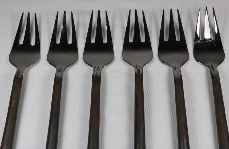 May include: Six silver forks with black handles. The forks are arranged in a row, with the handles pointing to the right.