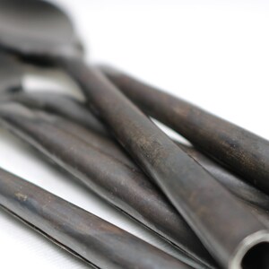 May include: A set of four black metal spoons with rounded ends. The spoons are arranged in a pile, with the handles overlapping.