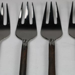 May include: Four silver forks with black handles. The forks are arranged in a row, with the handles pointing to the right.