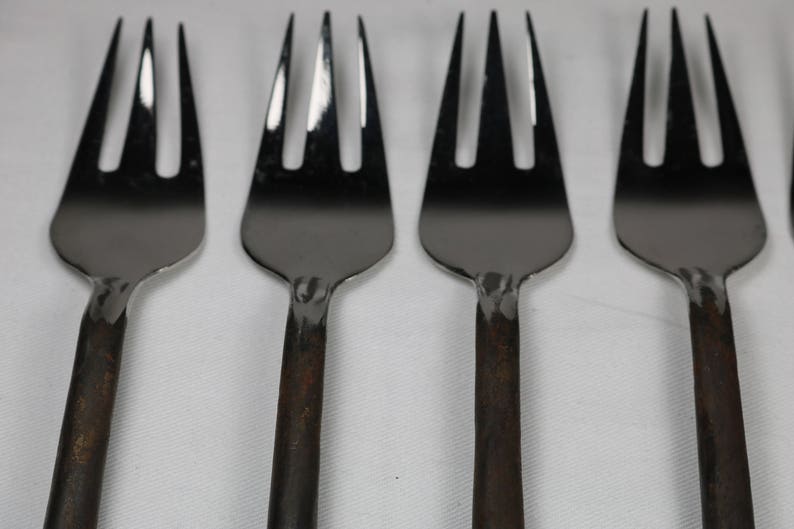 May include: Four silver forks with black handles. The forks are arranged in a row, with the handles pointing to the right.