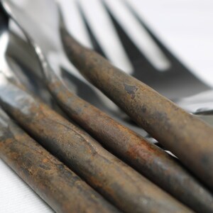 May include: Close-up of four forks with rusty handles. The forks are made of polished metal and have a classic design. The rusty handles are a unique and rustic detail.