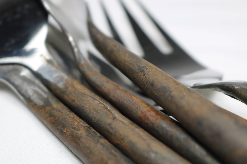May include: Close-up of four forks with rusty handles. The forks are made of polished metal and have a classic design. The rusty handles are a unique and rustic detail.