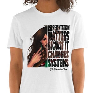Può includere: Maglietta bianca con un'illustrazione in bianco e nero di una donna con lunghi capelli castani. Il testo "Representation Matters Because It Changes Systems - Dr.  Femi  Akintola-  Tewo" è stampato sulla maglietta.