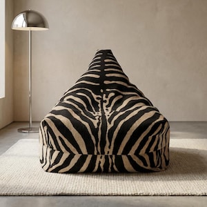 May include: A beanbag chair featuring a black and tan zebra print. The chair is triangular and sits on a light-coloured rug. A silver floor lamp is visible in the background. The chair is a statement piece.
