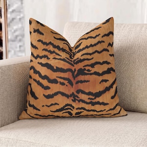 Peut inclure: Un coussin carré arborant un motif rayé de tigre aux nuances orange, marron et noir. Le design se compose de lignes noires horizontales, irrégulières et dentelées sur un fond aux tons chauds et variés d'orange et de marron.