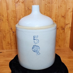 May include: A white ceramic crock with a blue and white label that reads "Buckeye Pottery Co. Blue Ribbon Stoneware,  Massillon, Ohio" and the number "5".