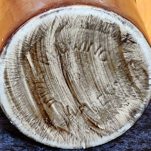 May include: Close-up of the bottom of a brown ceramic jar with a white glaze. The bottom of the jar has a handwritten inscription in brown ink.