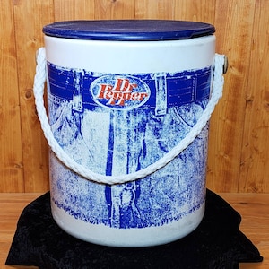 May include: White cooler with a blue and white Dr Pepper logo and a blue lid. The cooler has a white rope handle and a blue and white denim pattern.
