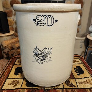 May include: A large, off-white stoneware crock with a rounded body and a wide rim. The crock features the number "20" in black script and a "Western Stoneware Plant 1" logo. It has two small handles on the sides.