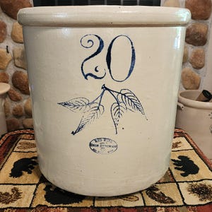 May include: A large, cylindrical, off-white stoneware crock featuring a prominent blue number 20 and a blue leaf design. Below the leaves, a blue oval stamp reads RED WING UNION STONEWARE CO. RED WING, MINN. The crock has a thick, rounded rim.