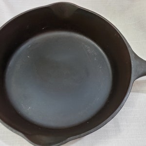 Op de afbeelding: Een zwarte gietijzeren koekenpan met een glad, licht verweerd oppervlak. De koekenpan heeft een lange steel en is ideaal om op het fornuis of in de oven te koken.