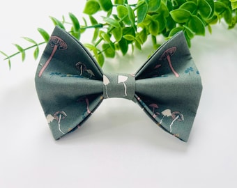 May include: A green bow tie with a mushroom print. The mushrooms are pink and white.