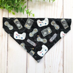 May include: Black dog bandana featuring a white and grey pattern of video game controllers and handheld game consoles.