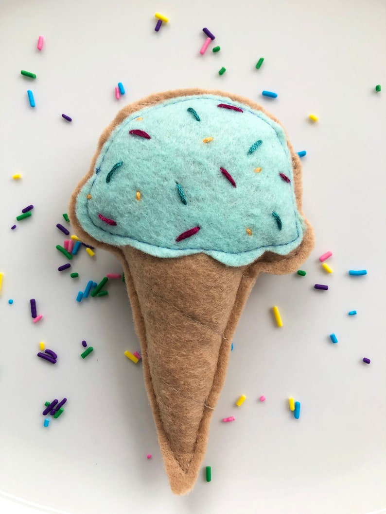 Puede incluir: Un cono de helado azul claro con chispas, hecho de fieltro. El cono es marr&oacute;n y el helado es azul claro con chispas de colores.