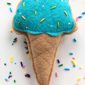 Puede incluir: Un cono de helado de fieltro azul con chispas amarillas y verdes. El cono est&aacute; hecho de fieltro marr&oacute;n y tiene una textura acolchada.