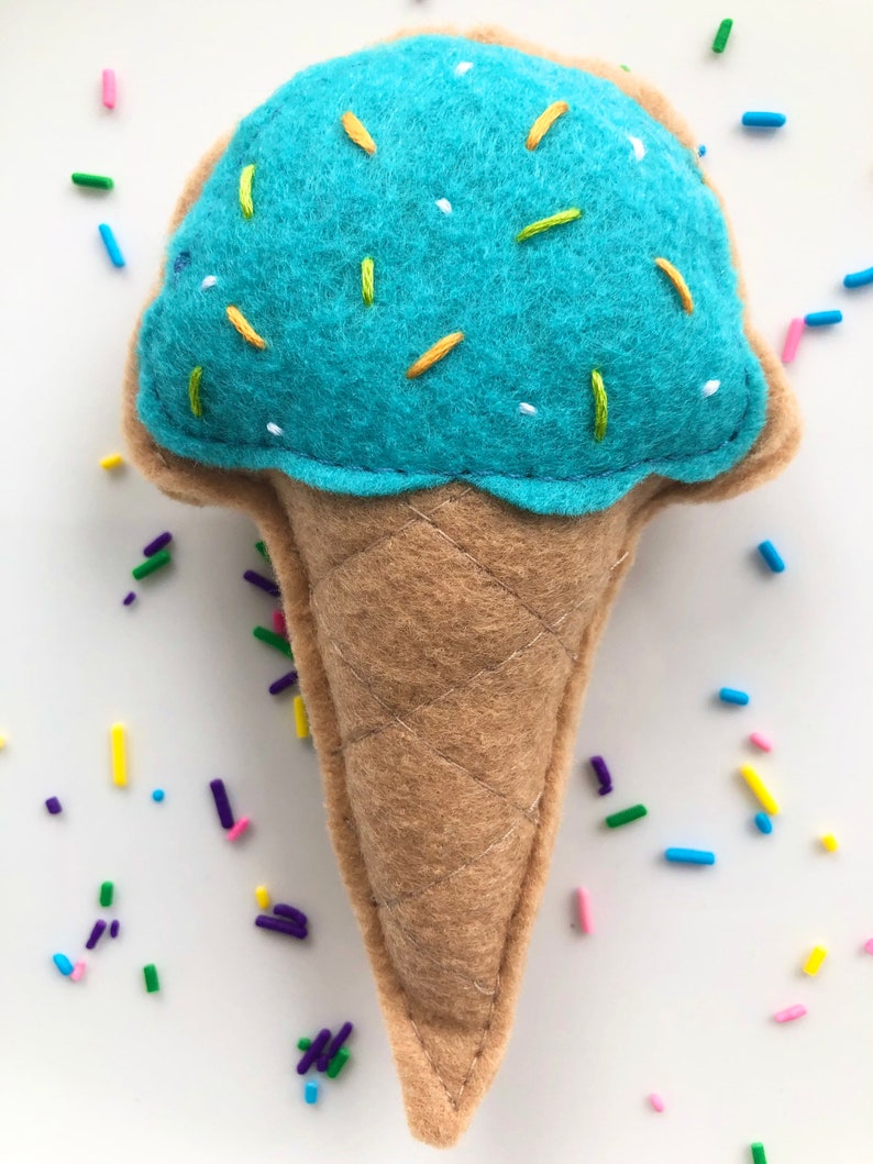 Puede incluir: Un cono de helado de fieltro azul con chispas amarillas y verdes. El cono est&aacute; hecho de fieltro marr&oacute;n y tiene una textura acolchada.