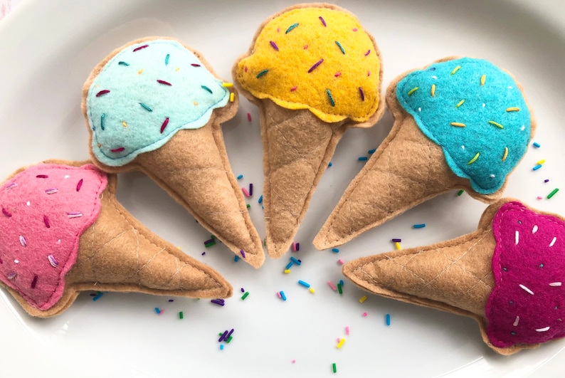 Puede incluir: Cinco conos de helado de fieltro con helados y chispas de diferentes colores. Los conos de helado son de color marr&oacute;n claro y el helado es rosa, amarillo, azul y azul claro.