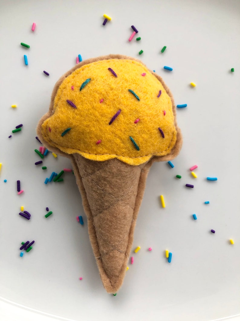 Puede incluir: Un cono de helado de fieltro amarillo con chispas de colores. El cono es marr&oacute;n y tiene una superficie texturizada.