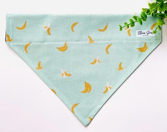 May include: A light blue bandana with a yellow banana pattern. The bandana has a white label with the text "Flora Soul Design".
