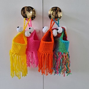 May include: Four crocheted monster-shaped pouches with googly eyes and fringe. The pouches are in yellow, orange, pink, and green.